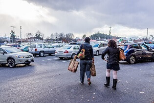 Two Shoppers with Bags Navigate a Busy Parking Lot